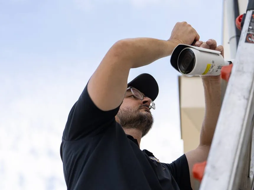 A technician on a ladder mounting a security camera on an exterior wall
